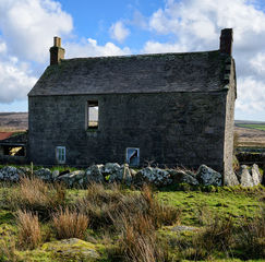 Old abandoned stone house with broken windows and overgrown land in a remote countryside setting